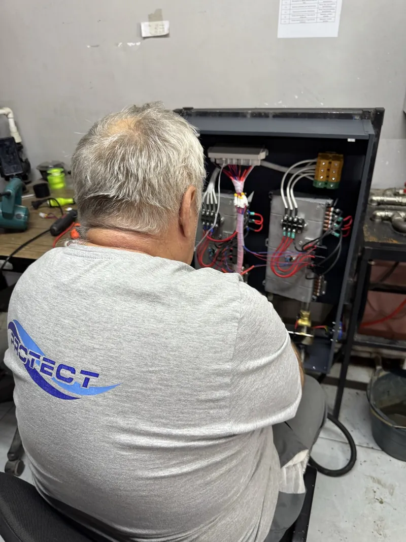 Мастер в футболке PROTECT собирает электрокотёл